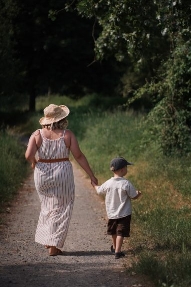 Eine Frau in einem Sonnenhut hält die Hand eines kleinen Jungen auf einem Weg.