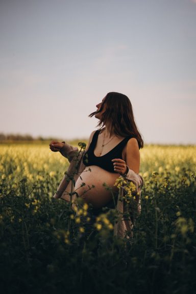Eine schwangere Frau steht in einem blühenden Feld und genießt die Natur.