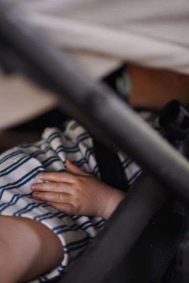 Ein kleines Kind mit gestreiftem Oberteil schläft in einem Kinderwagen.